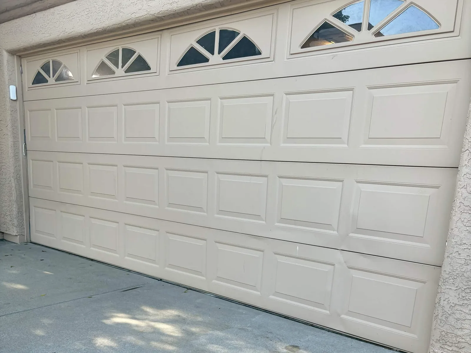 Before: aging almond raised-panel garage door with sunburst windows and dented lower panels in Mesa