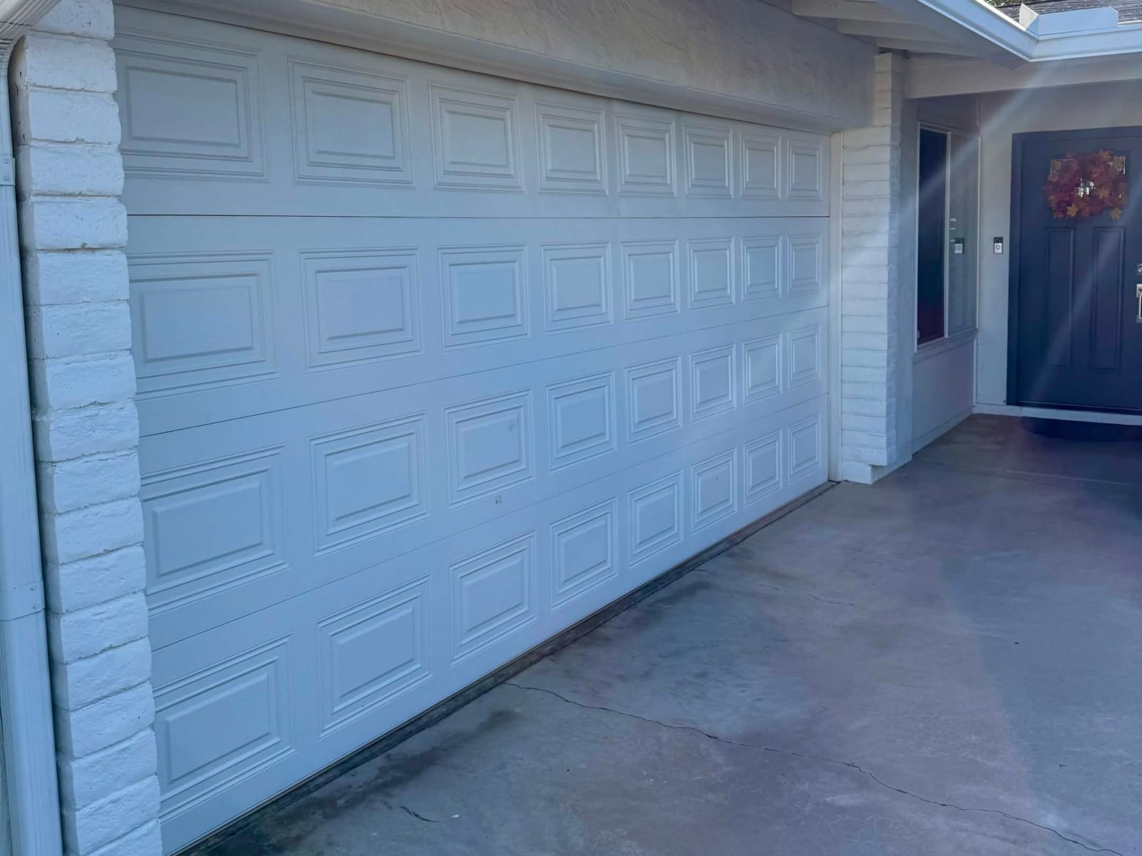 Before: old white raised-panel garage door, closed, with its top section damaged by a faulty opener, in Mesa