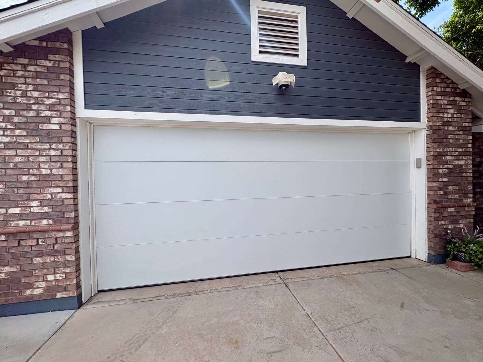After: new white flush-panel insulated double garage door on a brick and dark blue lap-siding garage in Mesa