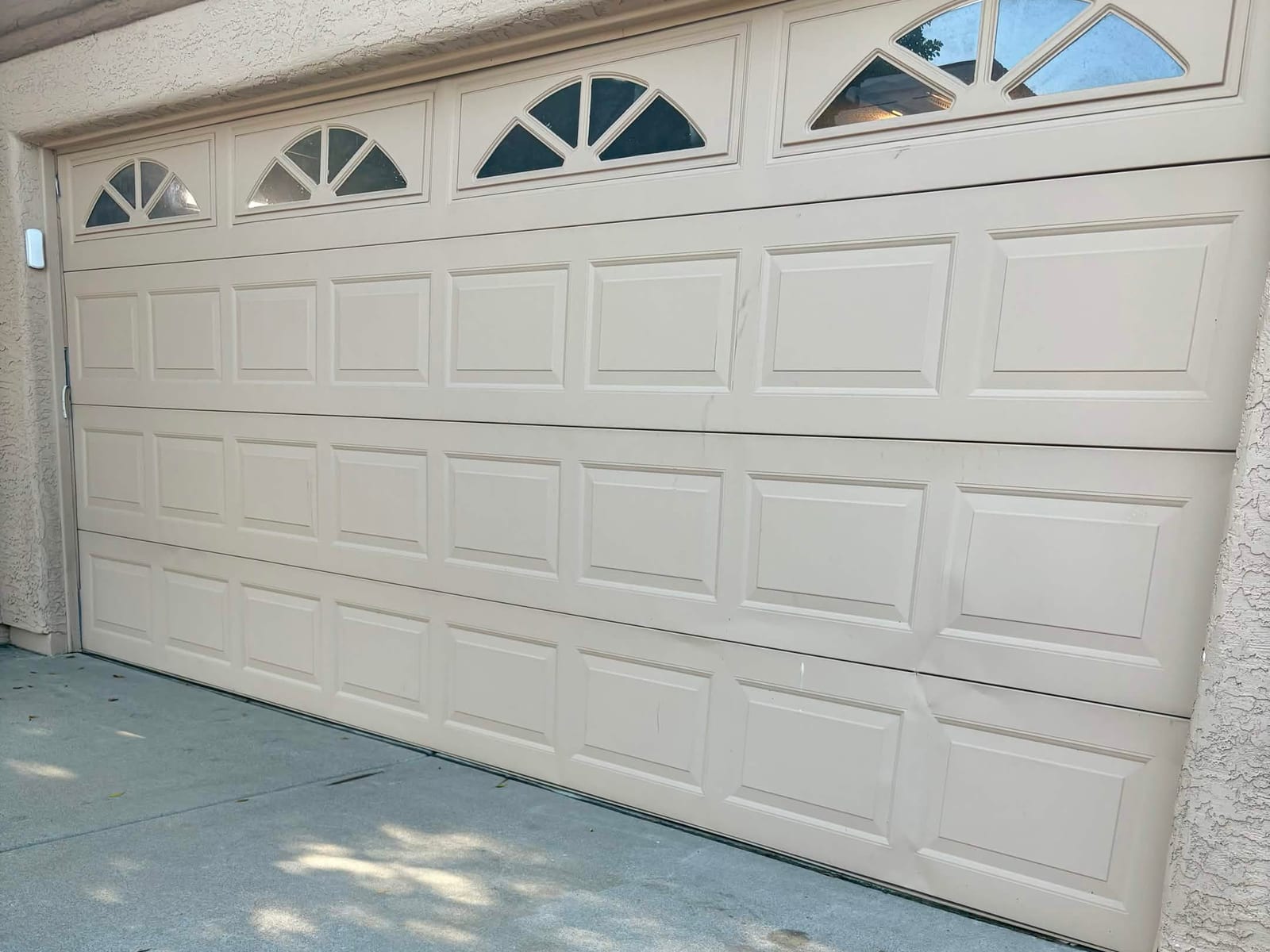 Before: 1980s almond raised-panel garage door with sunburst windows and dented lower panels in Alta Mesa