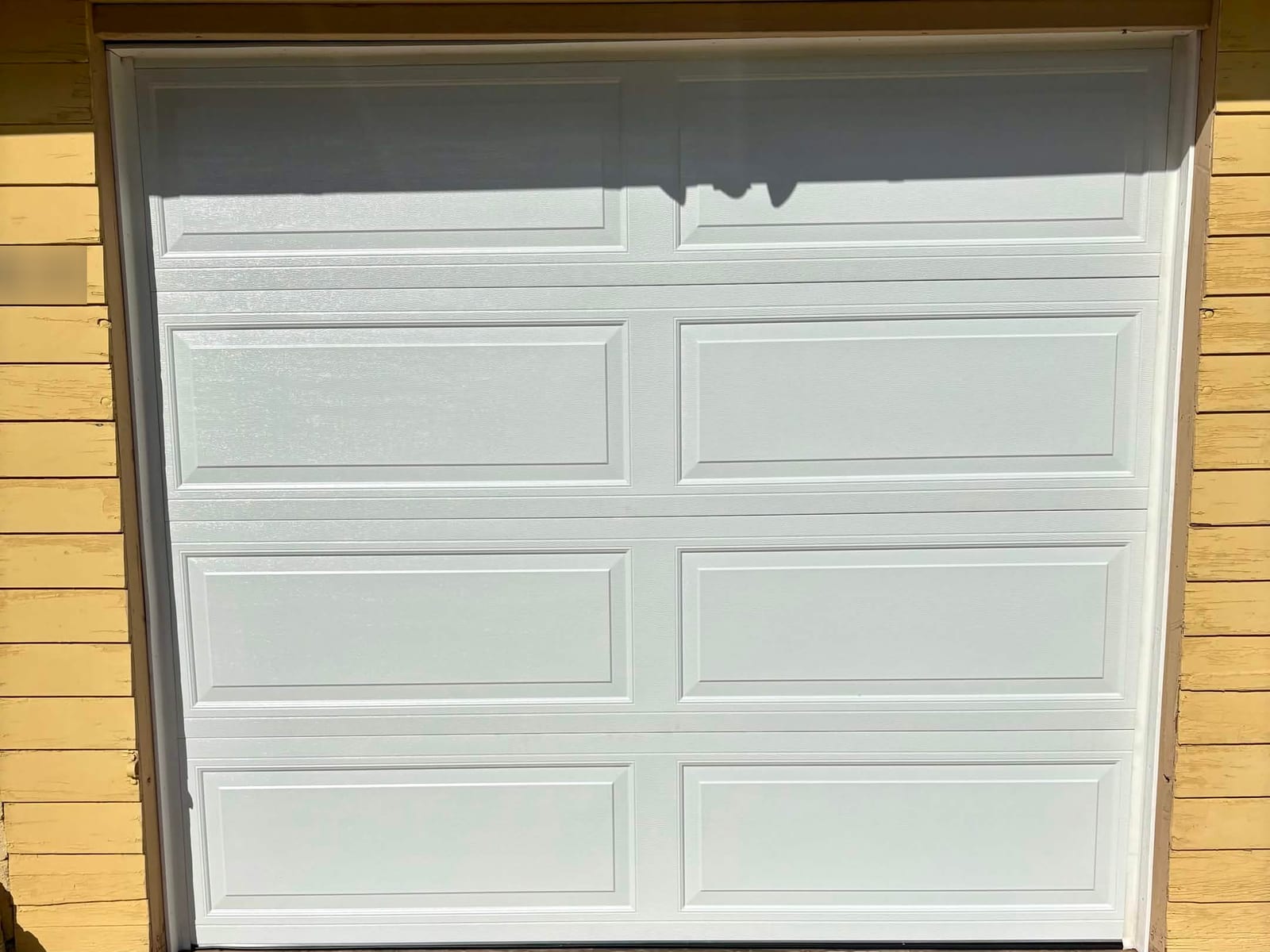 After: new white long-panel sectional garage door on a yellow-sided garage in Phoenix