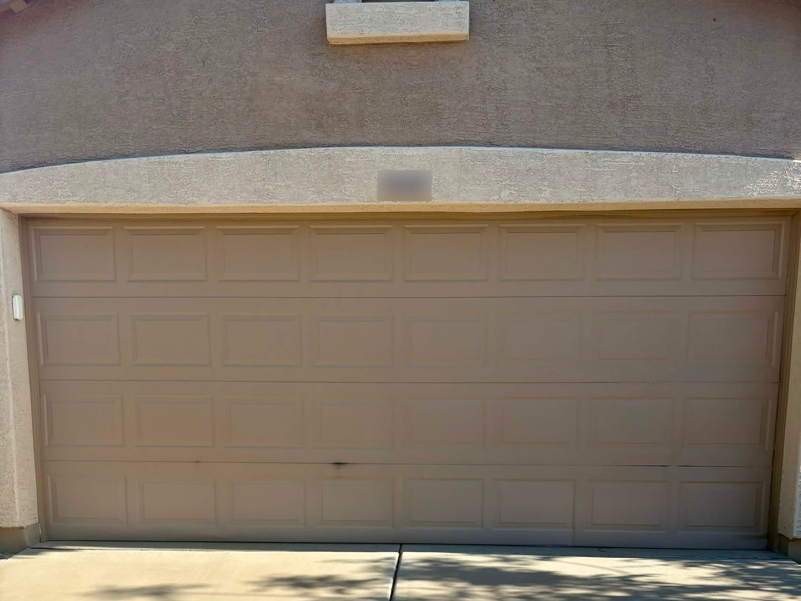 Before: tan raised-panel double garage door with damaged sections after being backed into, on a stucco home in Mesa
