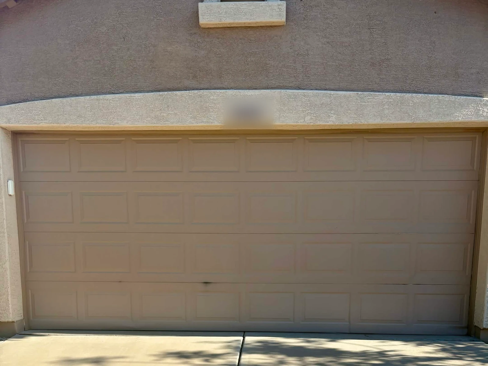 Before: tan raised-panel double garage door with damaged sections after being backed into, on a stucco home in Mesa